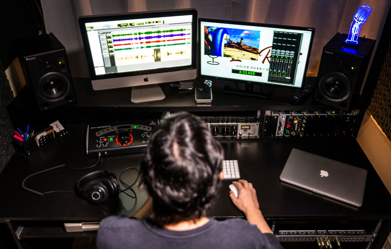 Seen from above, Leo is seated at the studio table in front of the computer and equipment. On screen the recording of a dubbing project for DisneyXD.